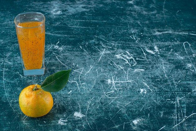 Mandarina y un vaso de jugo sobre fondo azul. Foto de alta calidad