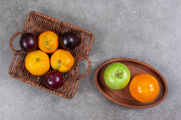 Mandarinas dulces frescas con ciruelas en una canasta de mimbre