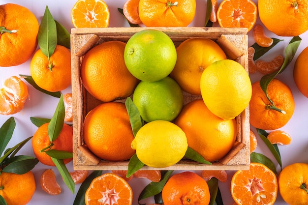 Foto gratuita mandarinas limones y frutas naranjas en caja de madera sobre superficie blanca