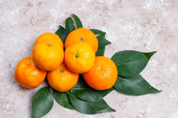 Mandarinas (naranjas, clementinas, cítricos) con hojas verdes en la superficie de concreto con espacio de copia