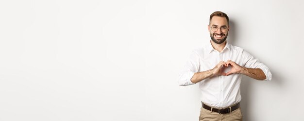 Manejar guapo mostrando el signo del corazón y sonriendo te amo gesto de pie sobre fondo blanco.