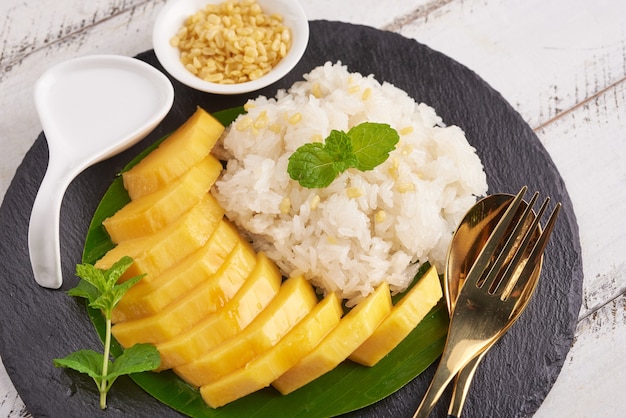 Mango maduro y arroz glutinoso con leche de coco en la superficie de la piedra, postre dulce tailandés en temporada de verano.