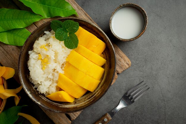 Mango maduro fresco y arroz pegajoso con leche de coco sobre superficie oscura