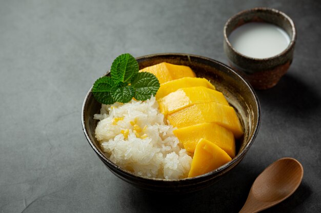 Mango maduro fresco y arroz pegajoso con leche de coco sobre superficie oscura