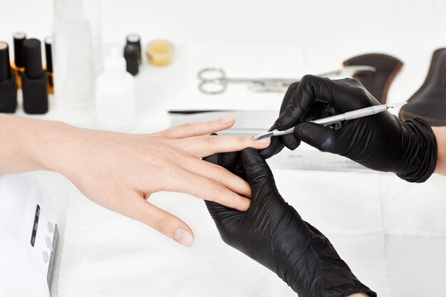 Manicurista en guantes empujando la cutícula en el dedo anular de la mujer.