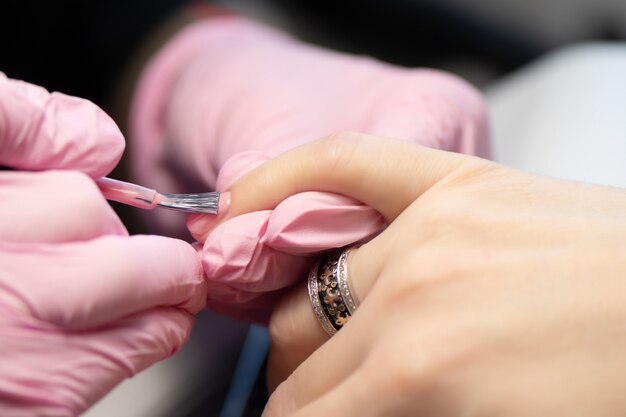 Manicurista haciendo gel diseño de uñas para el cliente, de cerca.