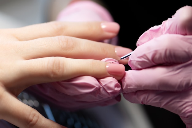 Manicurista haciendo gel diseño de uñas para el cliente, de cerca.