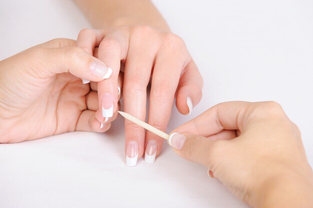 Manicurista haciendo limpieza de cutícula en los dedos femeninos con palo cosmético