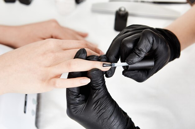 Manicurista profesional en guantes aplicando capa base en el dedo anular.