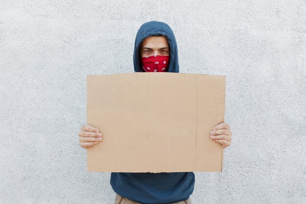 Manifestante decepcionado serio con pañuelo en la cara y cartón