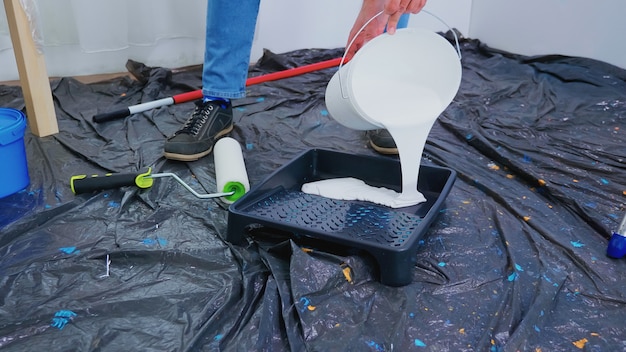 Manitas vertiendo pintura blanca para la renovación del hogar. Pareja en piso, reparación y cambio de imagen