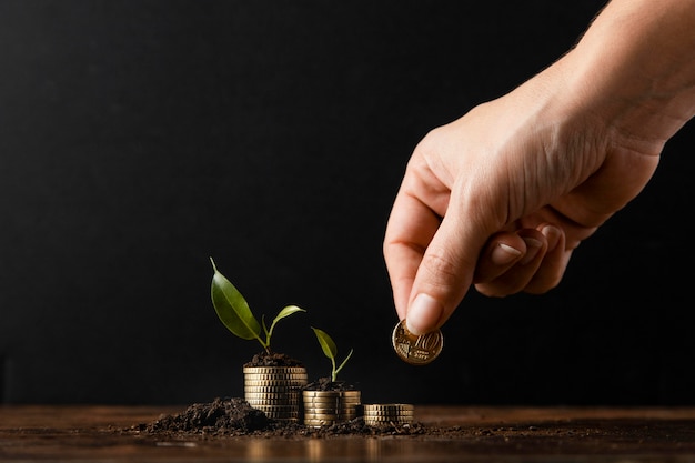 Foto gratuita mano agregando monedas para apilar cubiertas de tierra y plantas