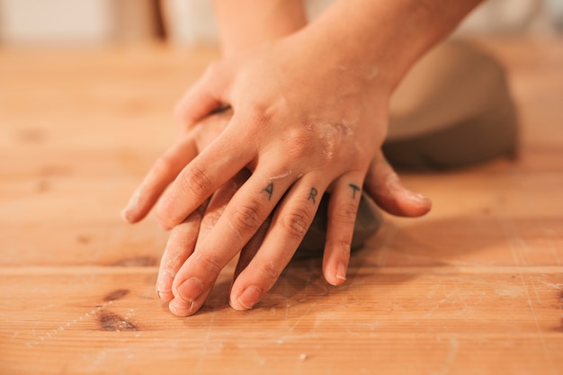 Mano de alfarero femenino amasando la arcilla en superficie de madera