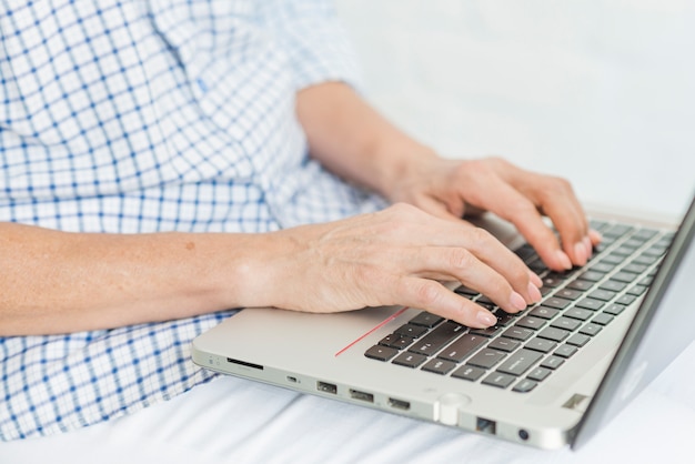 La mano de una anciana escribiendo en la computadora portátil portátil