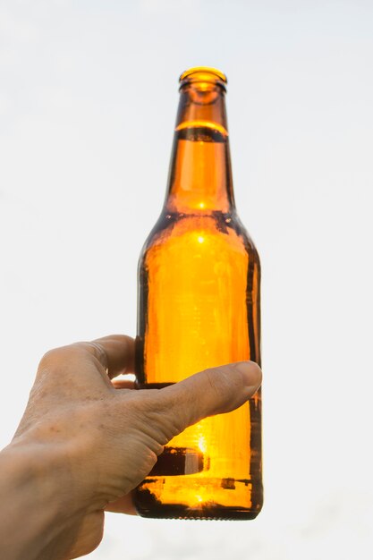 Mano de ángulo bajo con botella de cerveza abierta