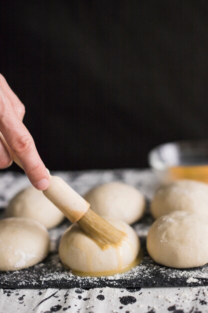 Mano aplicando la yema sobre los bollos crudos.