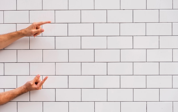 Foto gratuita mano apuntando a la pared de ladrillo blanco