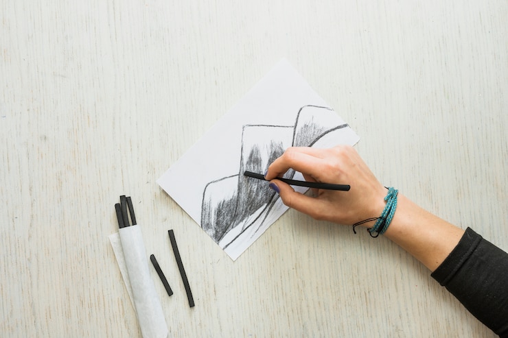Foto gratuito mano del artista dibujando un dibujo en papel blanco con palillo de carbón.