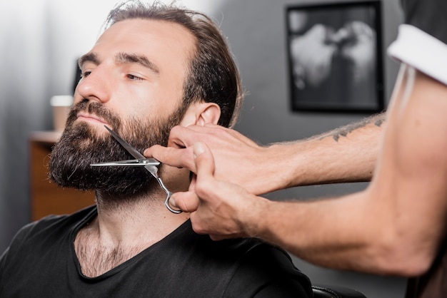 Mano de barbero que diseña la barba de hombre con tijeras