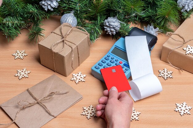 Mano de cajero sosteniendo una tarjeta de crédito sobre una máquina edc o caja registradora para pagar regalos de navidad en el mostrador con decoración navideña. concepto de venta de navidad