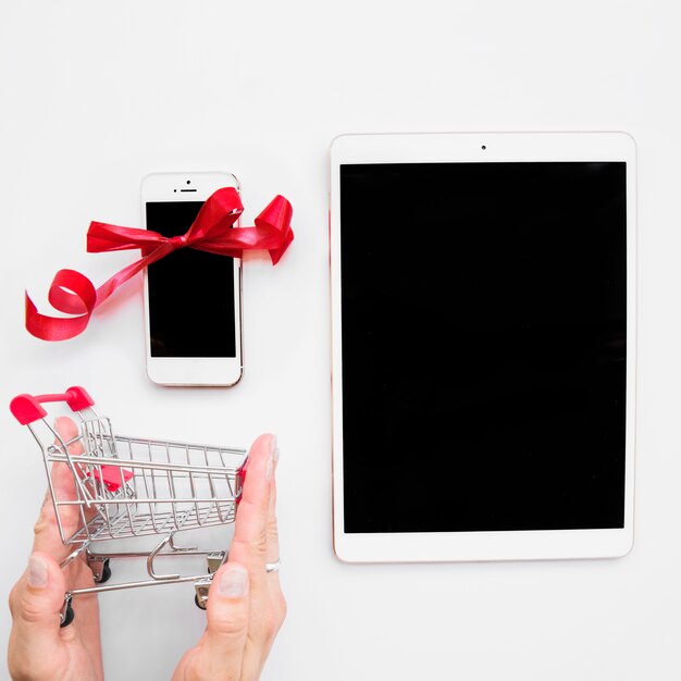 Mano con carrito de compras cerca de tableta y teléfono inteligente