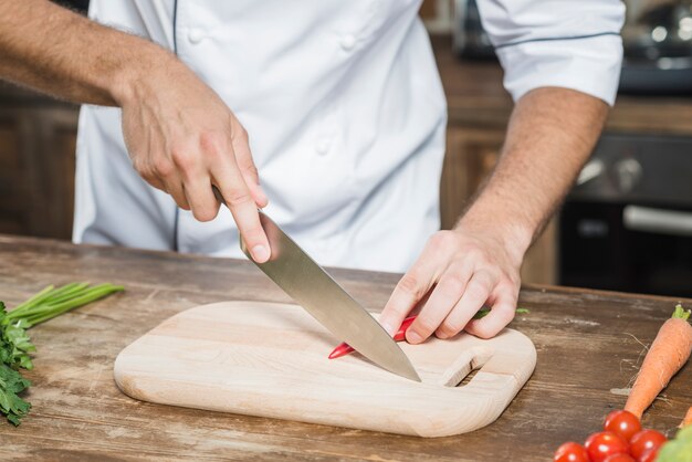 Mano del chef cortar chile rojo en tajadera