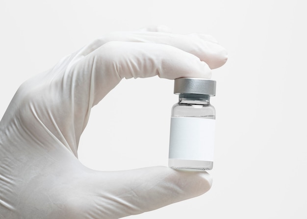 Mano del científico sosteniendo la botella de vidrio de medicina con etiqueta blanca en blanco