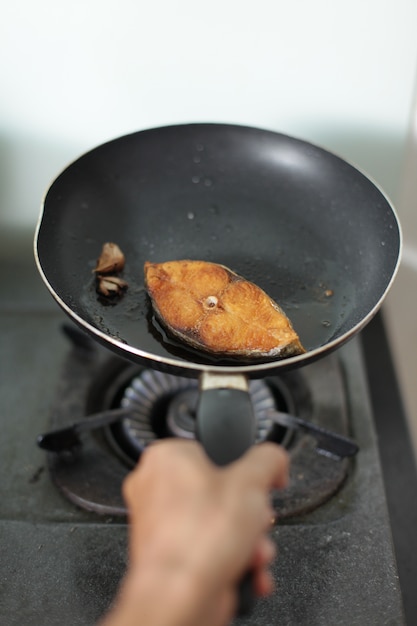 Mano cocinando pescado en una sartén