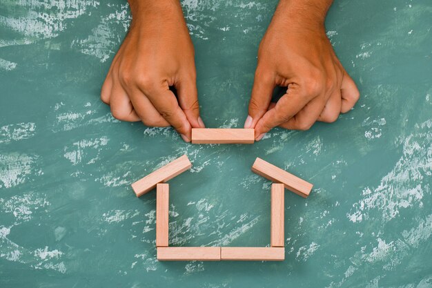 Mano construyendo casa con bloques de madera.