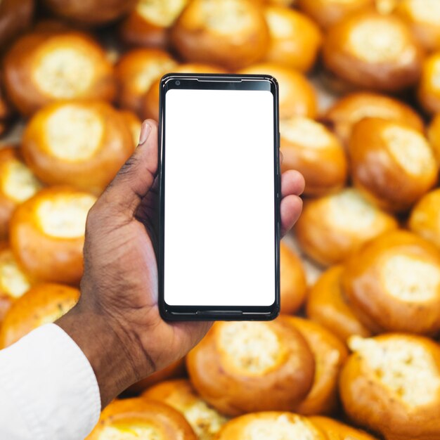 Mano de la cosecha con el teléfono inteligente en el fondo de pastelería