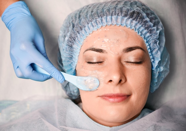 Mano cosmetóloga aplicando máscara cosmética en la cara de la mujer