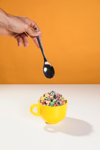 Foto gratuita de la mano con una cuchara para mezclar el tazón con leche y cereales.