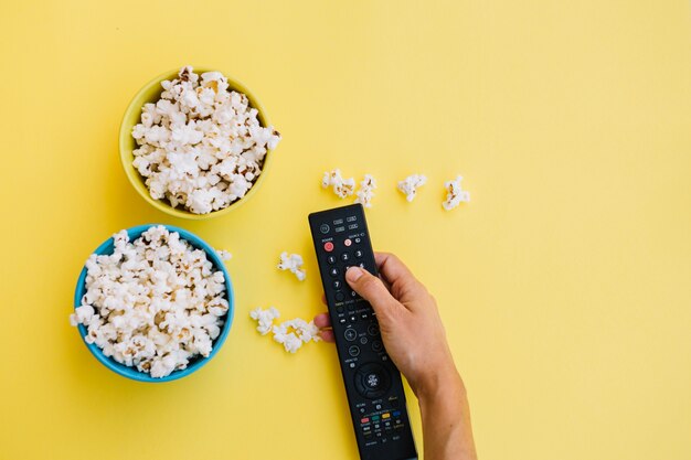 Mano de cultivo con control remoto cerca de palomitas de maíz