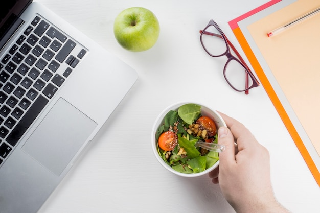 Mano de cultivo poniendo ensalada cerca de la computadora portátil