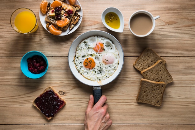 Foto gratuita mano de cultivo poniendo huevos fritos cerca de la comida del desayuno