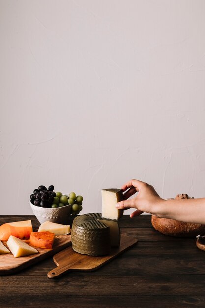 Mano de cultivo tomando pedazo de queso de la mesa