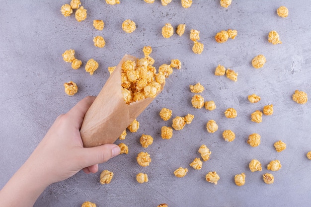 Una mano derramando un paquete de palomitas de maíz recubiertas de caramelo sobre fondo de mármol. Foto de alta calidad