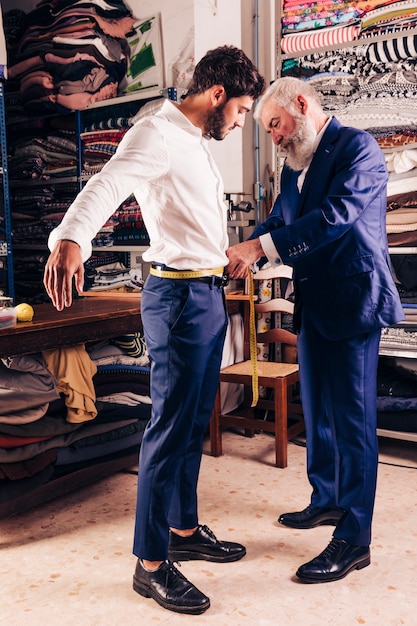 La mano del diseñador de moda masculino mayor que toma la medida de la cintura de su cliente con cinta métrica amarilla