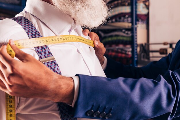 La mano del diseñador de moda que mide el pecho de su cliente con cinta métrica amarilla