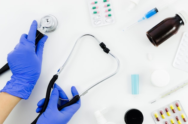 La mano del doctor con el estetoscopio y el equipamiento médico en el fondo blanco