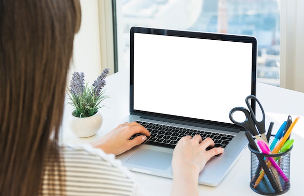 Mano de la empresaria usando laptop con pantalla blanca en blanco en el escritorio