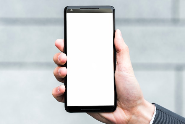 La mano de un empresario que muestra la pantalla blanca de un teléfono inteligente contra un fondo borroso