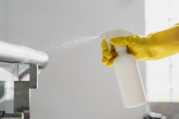 Mano enguantada de goma sosteniendo una botella de spray blanco