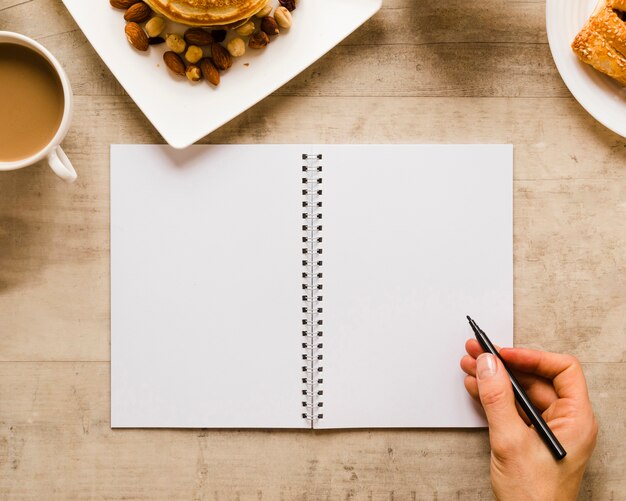 Mano escribiendo en cuaderno con café