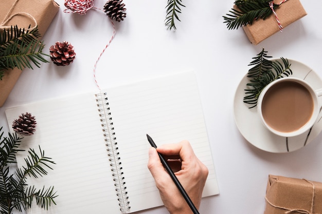 Mano escribiendo en el cuaderno cerca de bebidas calientes