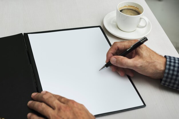 Mano escribiendo en papel en blanco junto a la taza de café