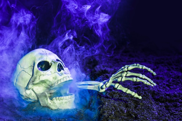 Foto gratuita mano de esqueleto de azul que sobresale de la calavera en el suelo