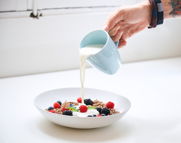 Foto gratuita mano estropea la leche de la taza azul al muesli en un plato blanco para el desayuno