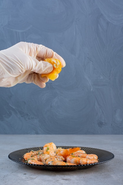 Foto gratuita mano exprimiendo limón en un plato de deliciosos camarones sobre un fondo de piedra.