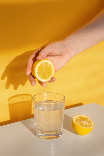 Mano exprimiendo limón en un vaso de agua de alto ángulo